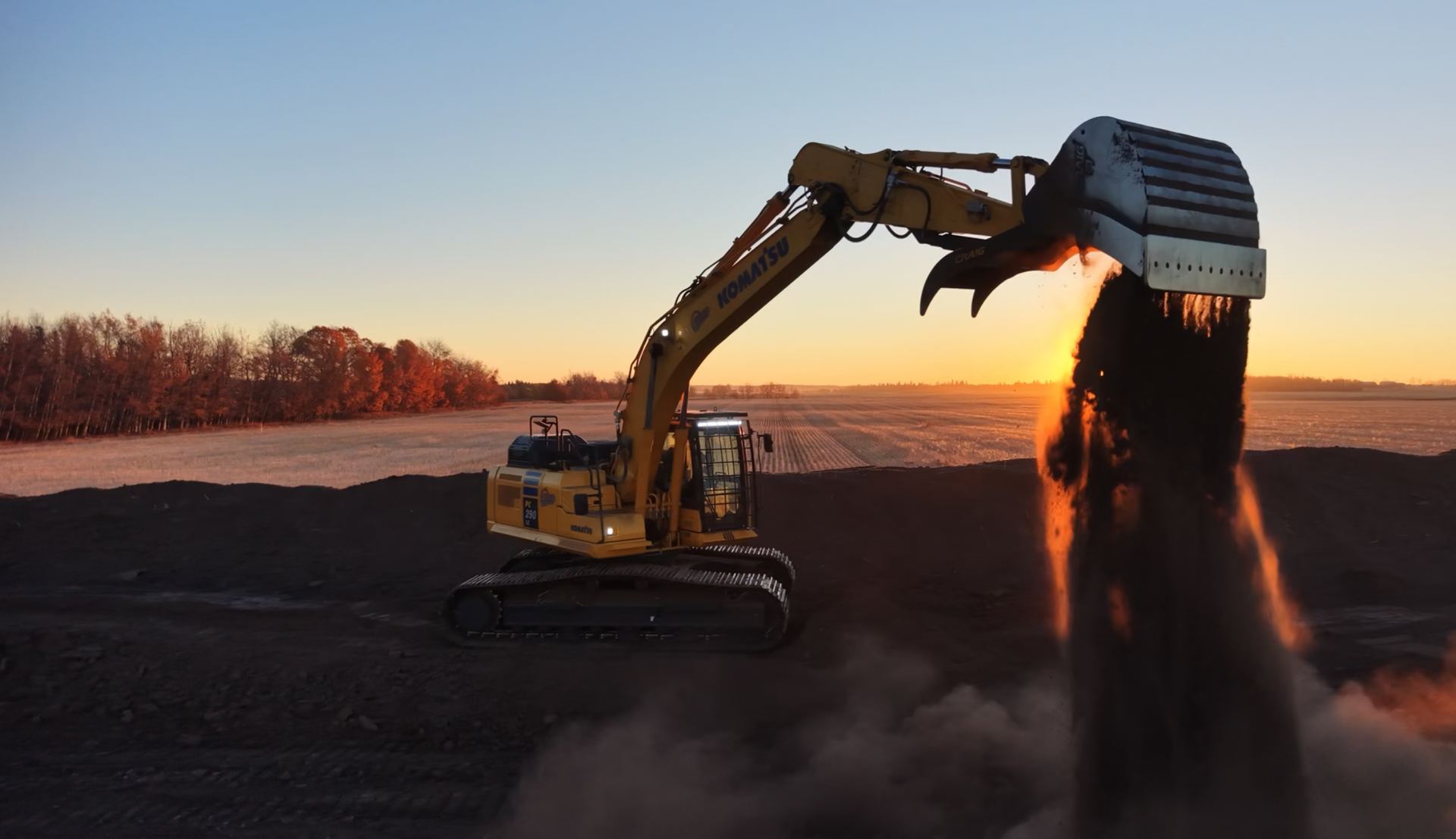 Excavator loading topsoil at sunset on an Alberta oilfield site